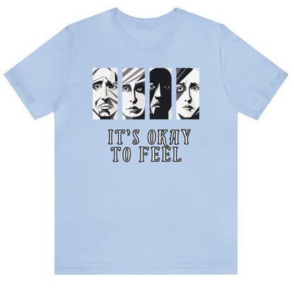 Baby blue mental health awareness t-shirt with four faces arranged horizontally across the shirt with the phrase 'It's Okay to Feel' below. Each face represents real emotions. Perfect for mental health advocates.