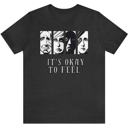 Dark grey heather mental health awareness t-shirt with four faces arranged horizontally across the shirt with the phrase 'It's Okay to Feel' below. Each face represents real emotions. Perfect for mental health advocates.