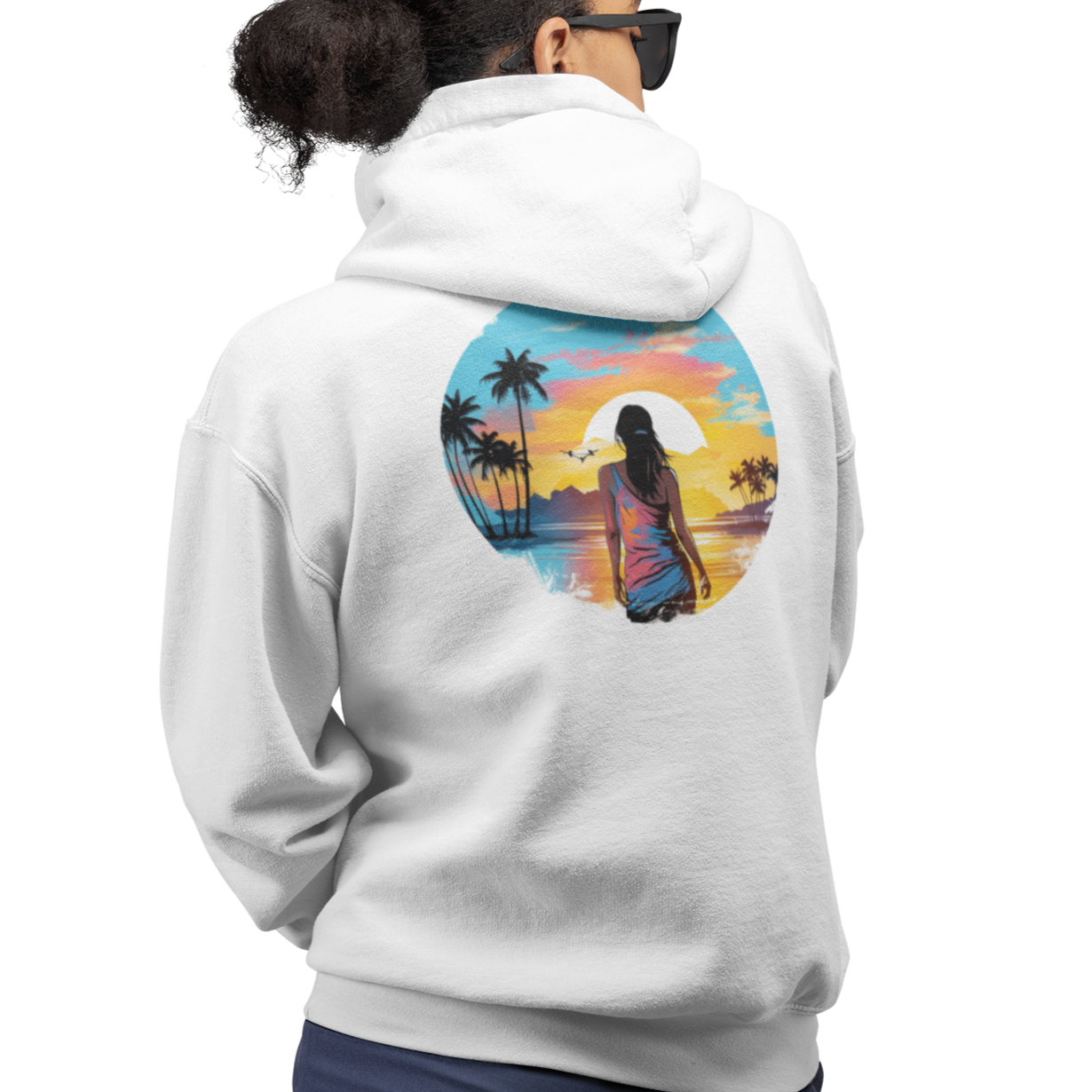 Back view of our 'Be Free' Beach Sunset Hoodie showing a graphic of a woman gazing out over a tranquil sunset at the water's edge. In the distance, palm trees and majestic mountains create a breathtaking backdrop. Perfect casual wear for a cool day on the beach, hiking, or everyday activities.