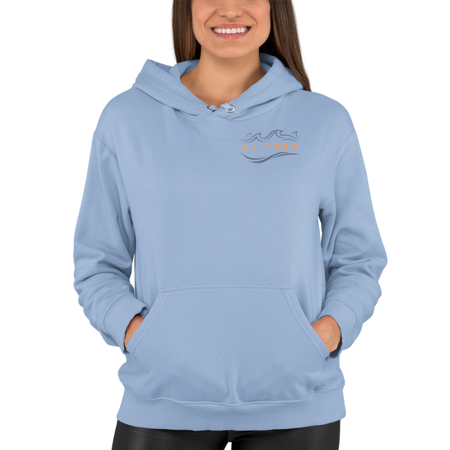 Woman wearing our light blue 'Be Free' Ocean Waves Hoodie showing the front logo with an ocean wave above the words 'Be Free' in an orange hue that matches the hoodie's full back graphic.