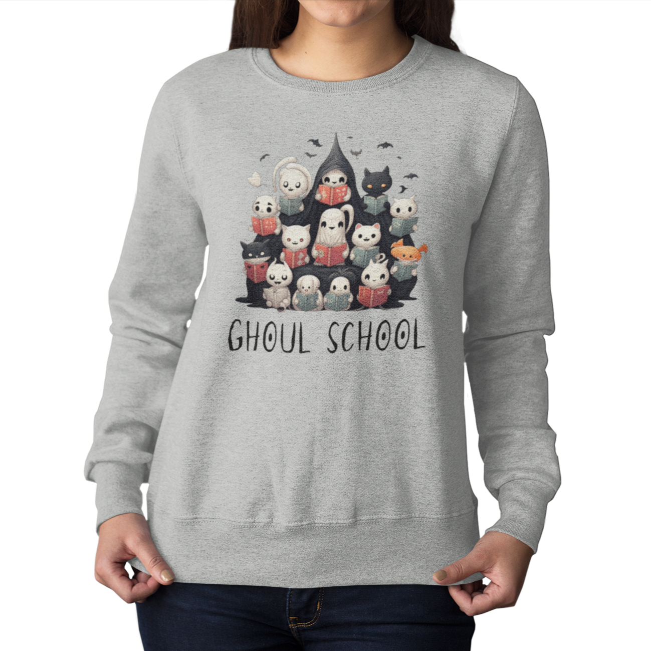 Woman wearing an Ash color Halloween 'Ghoul School' ghost sweatshirt. The graphic showcases a group of cute, stylish ghosts reading books, which creates a spooky classroom scene. The words 'Ghoul School' in a spooky font complete the look. Perfect for teachers, librarians, educators, students, and ghost lovers.