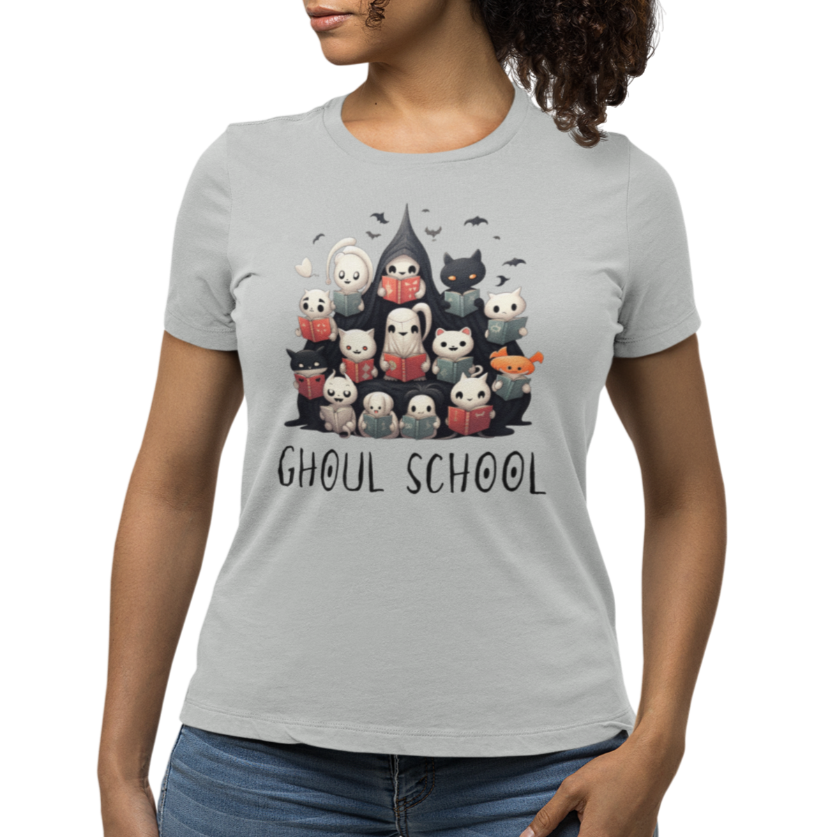 Woman wearing a grey Halloween 'Ghoul School' ghost t-shirt featuring a full graphic with cute ghosts reading books to create a spooky classroom scene. The caption 'Ghoul School' appears in spooky font. Unique t-shirt perfect for teachers, librarians, students, or anyone wanting to show off their Halloween school spirit. 